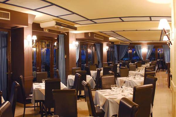 Innenansicht des Restaurants im Hersonissos Palace Hotel mit gedeckten Tischen und Stühlen, blauen Vorhängen und Lampen.