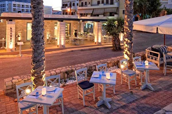Außenbereich des Hersonissos Palace Hotels mit beleuchteten Tischen und Stühlen unter einem großen Schirm.