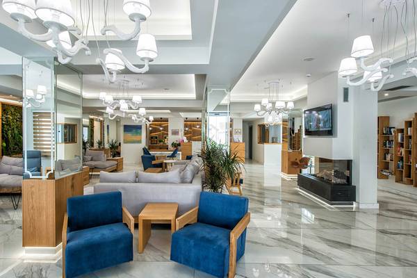 Lobby des Odyssia Beach Hotels mit modernen Möbeln, hellen Wänden und hängenden Kronleuchtern.