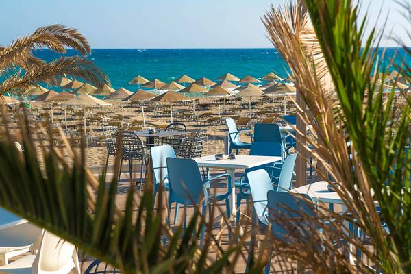 Blick auf die Terrasse des Odyssia Beach Hotels mit blauen Stühlen und Tischen am Strand