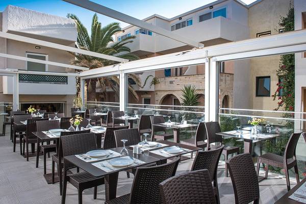 Terrasse des Odyssia Beach Hotels mit Tischen und Stühlen unter Glasdächern.