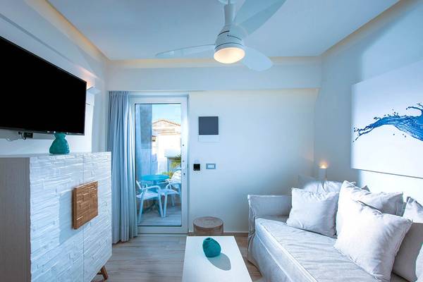 Wohnzimmer des Odyssia Beach Hotels mit Fernseher, Sofa, Tisch und Terrassentür.