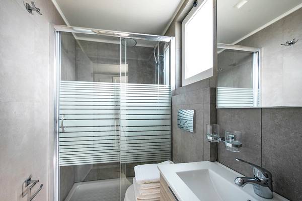 Badezimmer des Odyssia Beach Hotels mit einer Glasdusche, einem Waschbecken und einem Spiegel.