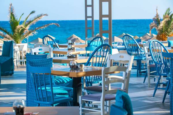 Außenbereich des Odyssia Beach Hotels mit Blick auf das Meer und blauen St ühlen.