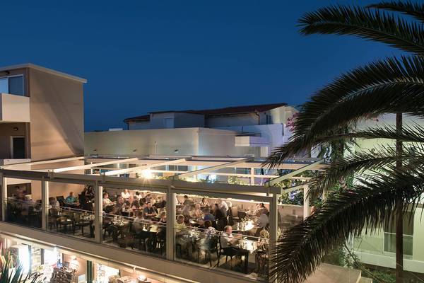 Abendessen auf der Terrasse des Odyssia Beach Hotels mit vielen Gästen und Palmen im Vordergrund.