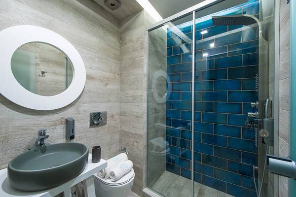 Badezimmer im Odyssia Beach Hotel mit blauen Fliesen, Dusche, Toilette und Waschbecken.