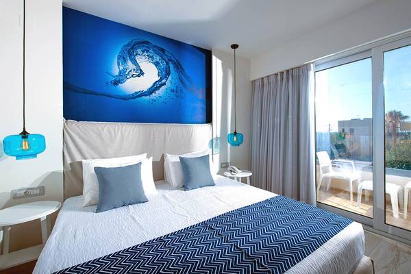 Schlafzimmer im Odyssia Beach Hotel mit blauer Wand, Doppelbett und großem Fenster.