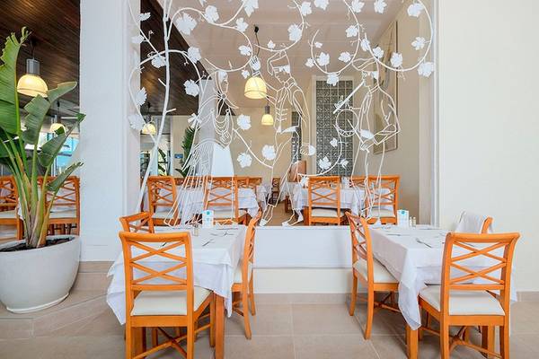 Restaurantbereich im Azuline Hotel Mar Amantis mit weißen Tischen, orangen Stühlen und Blattmustern an der Wand.