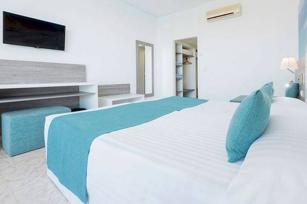 Schlafzimmer im Azuline Hotel Mar Amantis mit weißem Bett, blauen Kissen und Decken, Fernseher an der Wand, Schrank und Lampe.