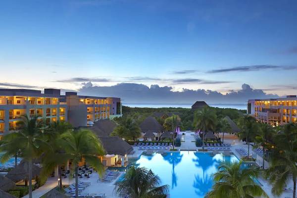 Außenansicht des Paradisus Playa del Carmen Hotels mit Pool und Gebäuden bei Sonnenuntergang.