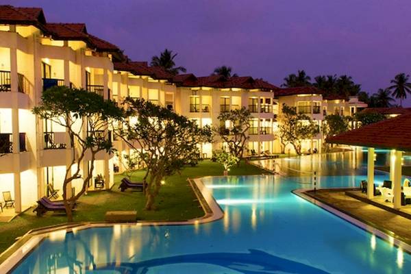 Abendliche Ansicht des Club Hotel Dolphin mit beleuchtetem Swimmingpool und geparkten Fahrzeugen.