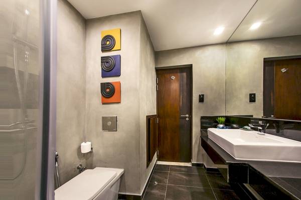 Badezimmer im Club Hotel Dolphin mit grauen Wänden, schwarzen Fliesen, weißem Waschbecken, Toilette und drei farbigen Wandbildern.