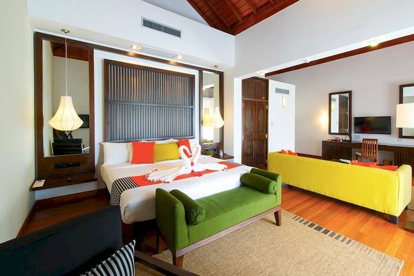 Innenansicht eines Zimmers im Club Hotel Dolphin mit Bett, Sofas, Lampen und Holzboden.