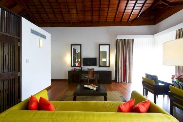Innenansicht des Wohnbereichs im Club Hotel Dolphin mit gelbem Sofa, rote Kissen, schwarzem Tisch und Spiegeln.