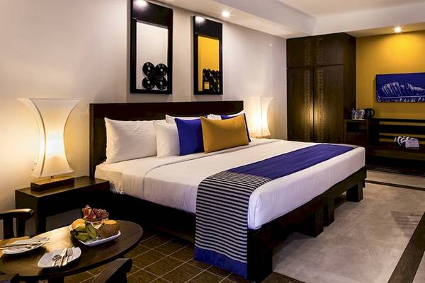 Innenansicht eines Zimmers im Club Hotel Dolphin mit einem großen Bett, Tisch, Stühlen und Früchten.