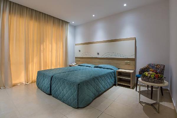 Doppelzimmer im Stamatia Hotel mit zwei Betten, neben einem Tisch mit Blumen und einer Wandlampe.