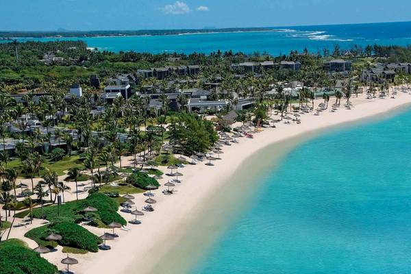 Luftaufnahme des Long Beach Mauritius Resorts mit weißem Sandstrand, türkisfarbenem Wasser und vielen Gebäuden.
