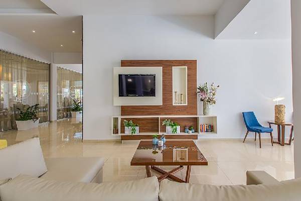 Modernes Wohnzimmer im Stamatia Hotel mit weißem Sofa, Glastisch und Fernseher an der Wand.