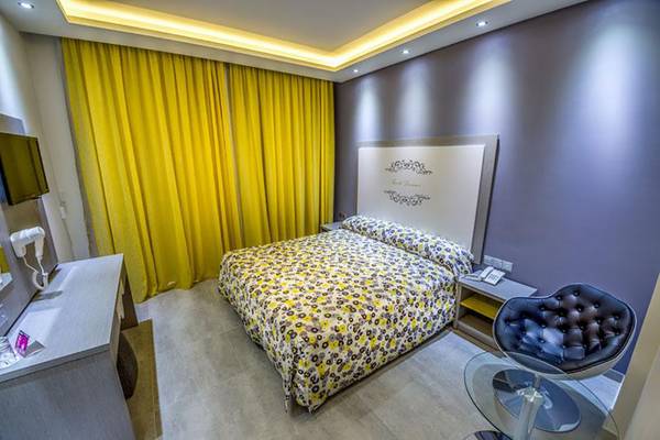 Innenansicht eines Hotelzimmers im Stamatia Hotel mit Bett, Nachttischen und gelben Vorhängen.