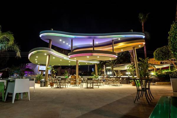 Außenbereich des Stamatia Hotels bei Nacht mit beleuchteter Dachstruktur und Tischen und Stühlen.