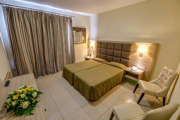 Doppelbett-Zimmer im Stamatia Hotel mit grünen Laken, zwei Nachttischen und einem Blumenstrauß auf dem Tisch.