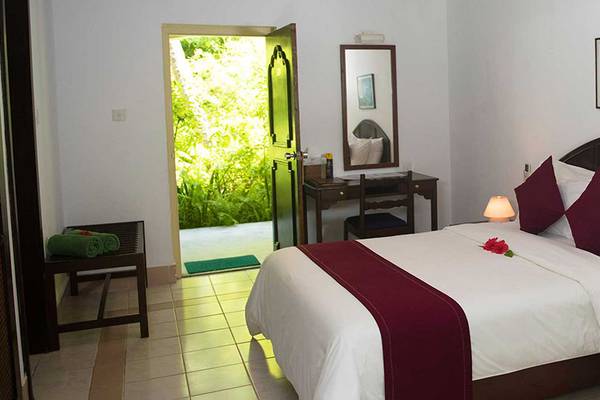 Innenansicht eines Schlafzimmers im Biyadhoo Island Resort mit einem Bett, Nachttischen und einem offenen Balkon.