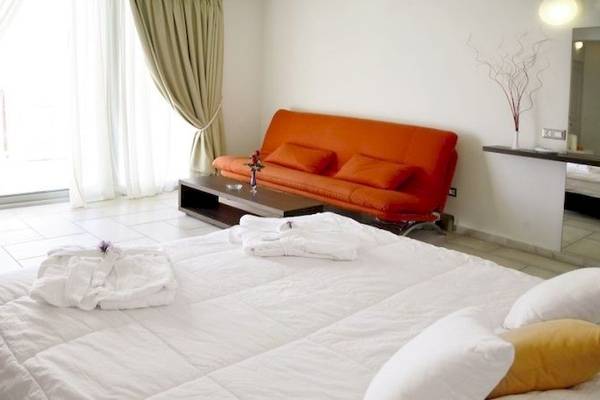 Schlafzimmer im Antinea Suites & Spa Hotel mit einem großen Bett, einem orangefarbenen Sofa und einer Glastür.
