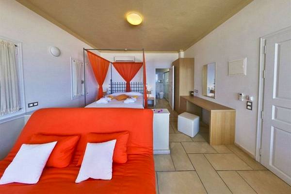 Hotelzimmer mit orangem Sofa und Bett, beide mit weißen Kissen, und rotem Vorhang.