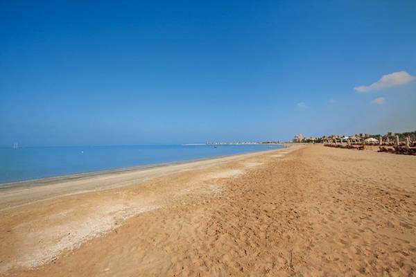 Strand des Waldorf Astoria Ras Al Khaimah Hotel mit blauem Himmel und ruhigen Wellen.