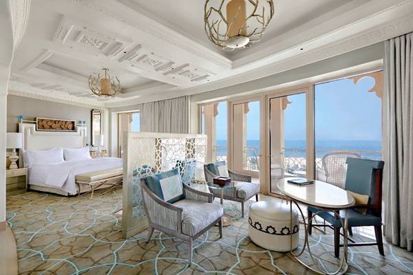 Innenansicht der Suite im Waldorf Astoria Ras Al Khaimah mit Bett, Sesseln, Tisch und Meerblick.