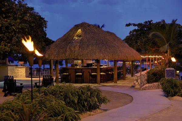 Ein Abendbild der Strandbar im Dreams Curacao Resort, Spa & Casino mit einem strohgedeckten Dach, brennenden Fackeln und stimmungsvollen Lichtern.