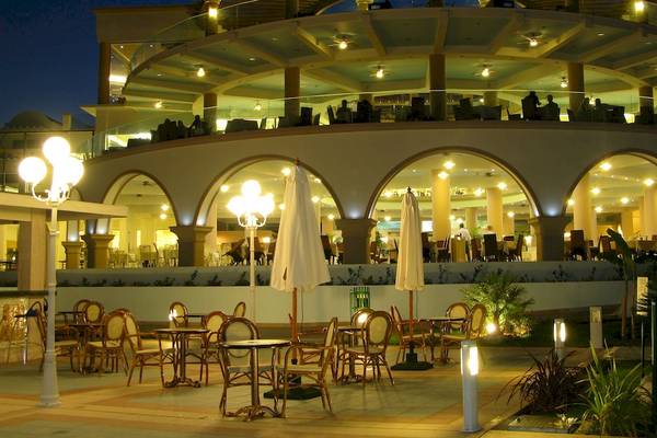 Abendansicht des Atrium Prestige Thalasso Spa Resorts & Villas mit beleuchteten Arkaden und gefüllten Tischen und Stühlen draußen.