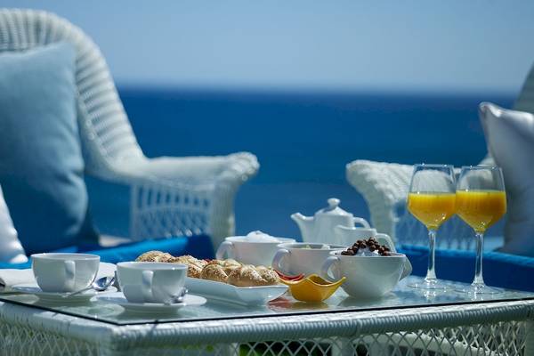Frühstück am Meer mit Blick auf das Meer, serviert auf einem Glastisch mit zwei Gläsern Orangensaft und einem Teller mit Croissants.