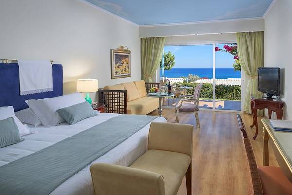 Ein modernes Hotelzimmer mit Meerblick, einem großen Bett, einem Wohnzimmerbereich und einem Esstisch auf der Terrasse.