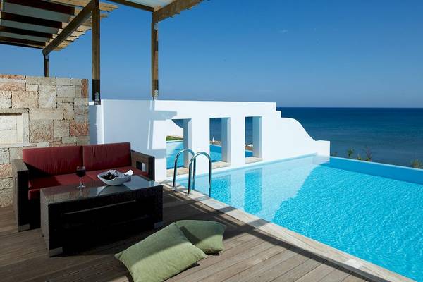 Außenpool des Atrium Prestige Thalasso Spa Resorts mit Blick auf das Meer und einer Loungeecke mit roten Kissen.
