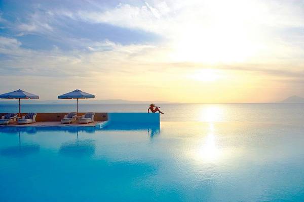 Ein Swimmingpool am Meer mit einer Person, die auf der Kante sitzt, während die Sonne untergeht.