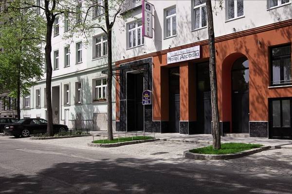 Außenansicht des Hotel Arcadia mit rotem Gebäudeteil und Bäumen auf der Straße.