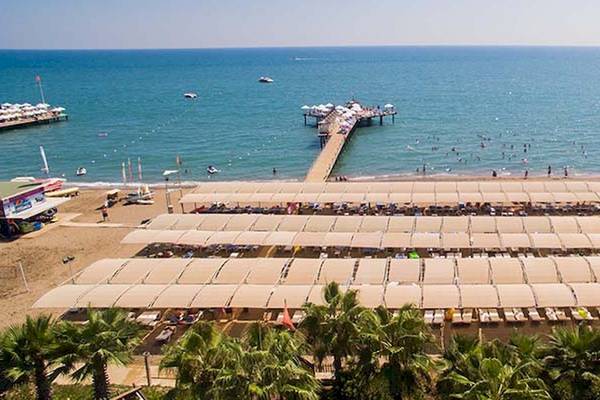 Luftaufnahme des Saturn Palace Resorts Strands mit mehreren Sonnenschirmen und Liegen.