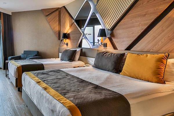 Zwei Betten mit gelben und grauen Kissen in einem modernen Hotelzimmer des Saturn Palace Resort.