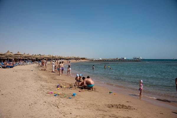 Sandstrand mit vielen Menschen und Sonnenschirmen, einige spielen im Sand und andere schwimmen im Wasser