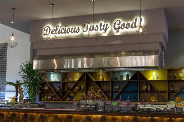 Inneneinrichtung des Ali Baba Palace Hotels mit einem Schild, das 'Delicious Tasty Good' beleuchtet, und einer Theke voller Speisen.