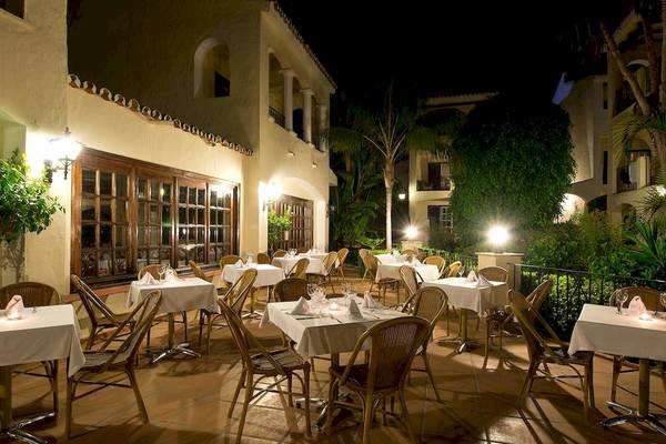 Außenbereich des Bluebay Banus Hotel Restaurants bei Nacht mit illuminierten Tischen und Stühlen.