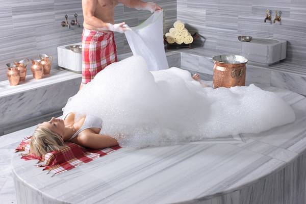 Eine Frau liegt in einem Schaumbad im Rixos Premium Dubrovnik, während ein Mann neben ihr steht.