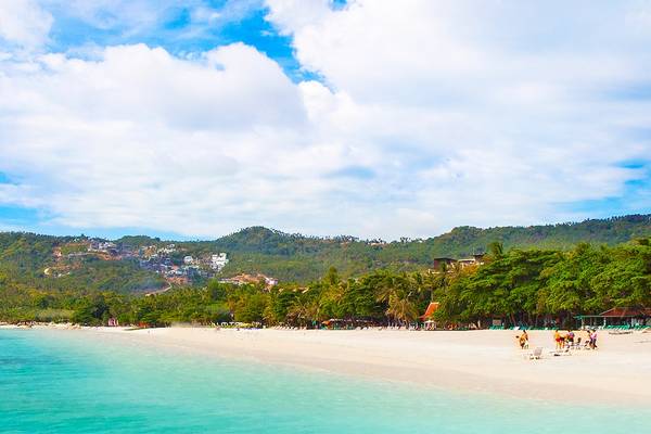 Eine weiße Strand mit Palmen und einem Bergpanorama im Hintergrund.