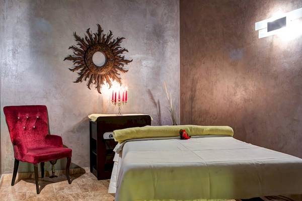 Behandlungsraum im Rixos Premium Dubrovnik mit einem roten Stuhl, einem Bett und Kerzen.