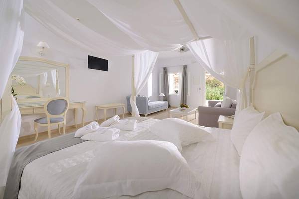 Ein modernes, helles Schlafzimmer mit einem großen Bett, weißen Vorhängen und Möbeln im Kamari Hotel.