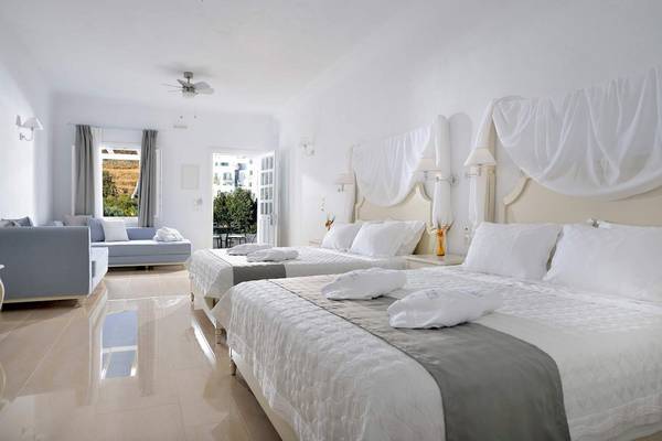 Schlafzimmer im Kamari Hotel mit zwei Betten, Couch, Fenster und Deckenventilator.