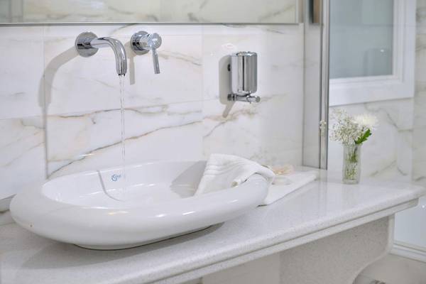 Ein Badezimmer mit einem weißen Waschbecken, das an eine Wand mit Marmorfliesen angeschlossen ist.