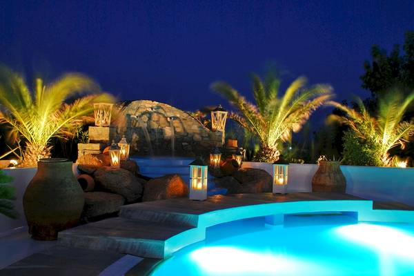 Außenbereich des Kamari Hotels bei Nacht mit beleuchtetem Pool und Steinmauer.