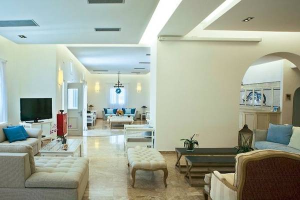 Wohnbereich des Kamari Hotels mit modernen Möbeln, Fernseher, Sofas, Couchtischen und Pflanzen.